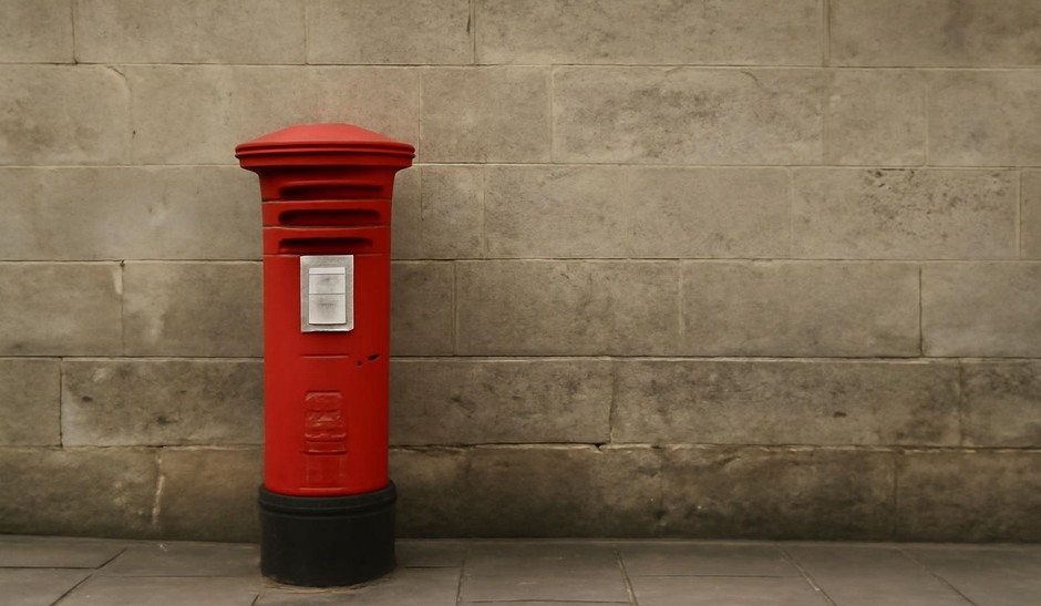 A small bright red postbox against a muted stone wall, framed with negative space